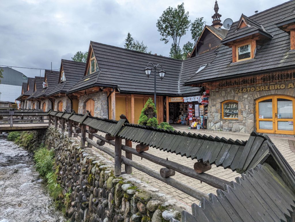 Petits magasins en brique et en bois avec une rivière et un pont devant à Zakopane pendant notre roadtrip en pologne © Le Voyage de FloLili - Blog de Voyage